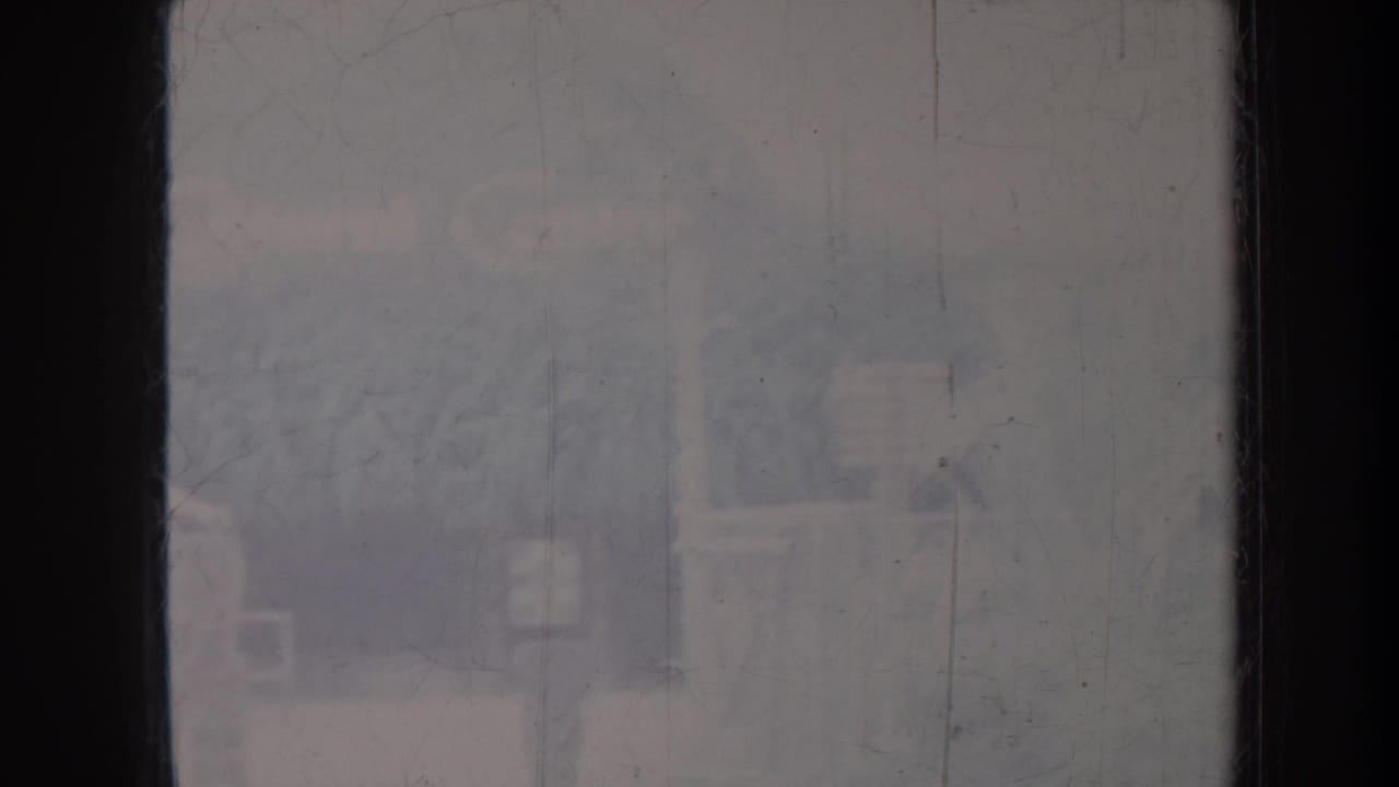 Blurred view through a dark-framed window with faint exterior structures beyond.