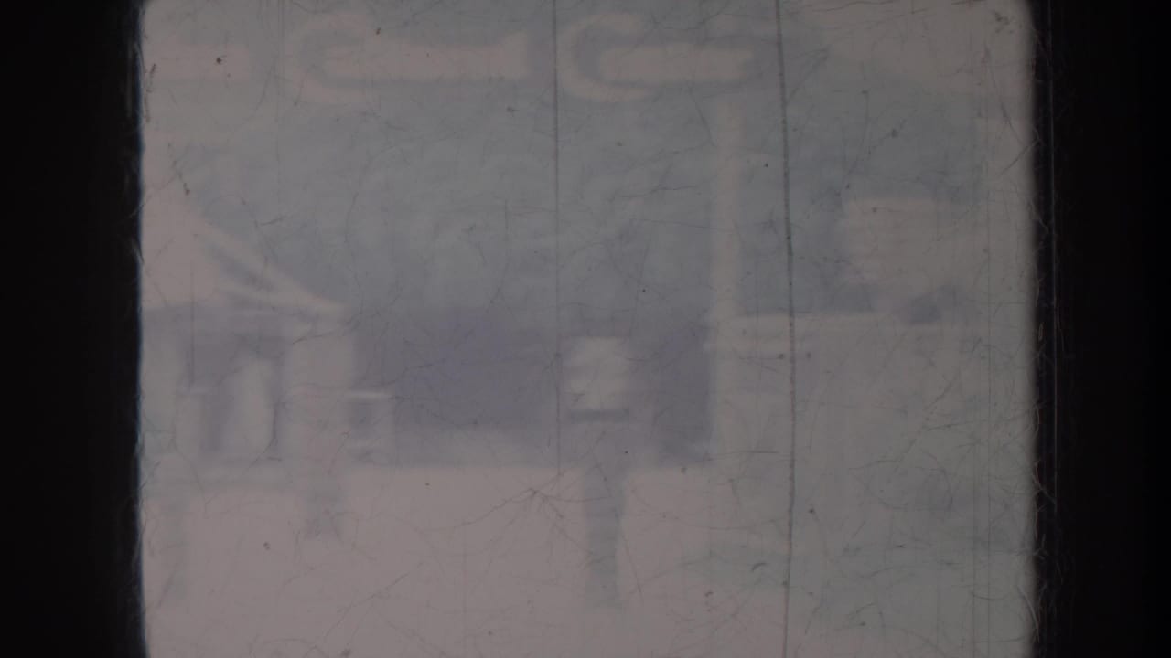 Hazy Honolulu home-movie frame with a dark vertical mullion and indistinct building shapes beyond glass.