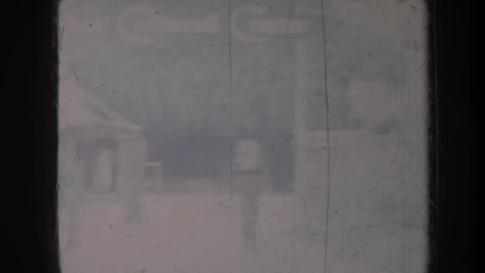 Hazy Honolulu home-movie frame with a dark vertical mullion and indistinct building shapes beyond glass.