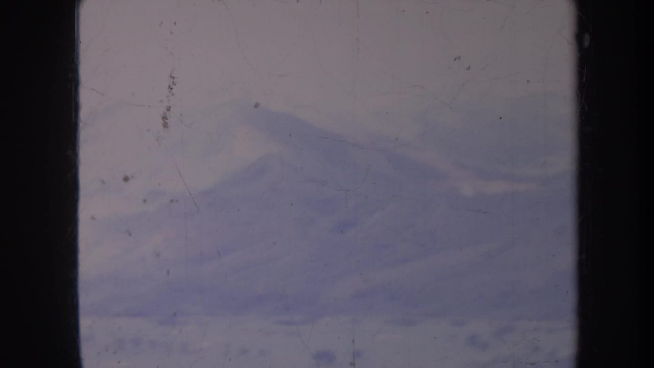 Hazy blue-purple mountain range beneath a pale sky with heavy film dust and scratches.