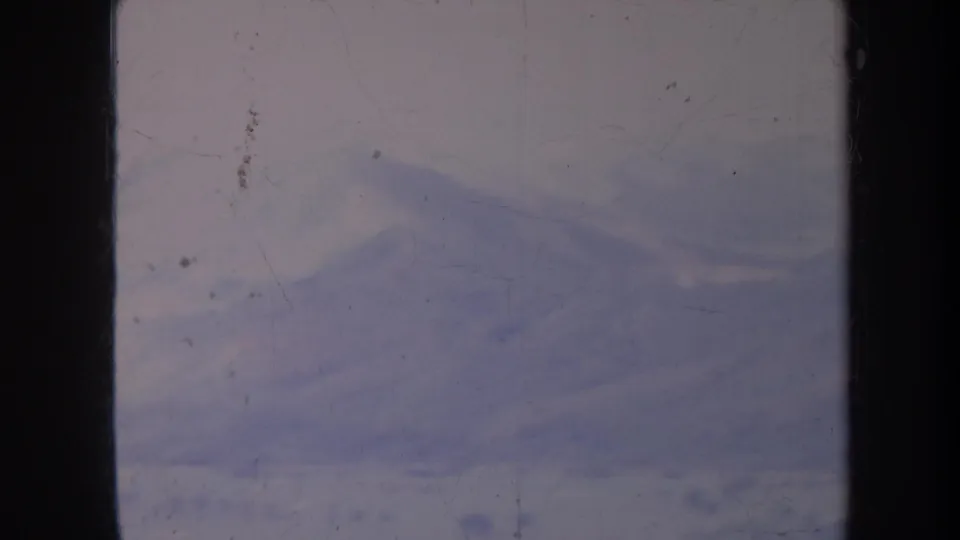 1967 Honolulu 8mm frame showing a distant hazy mountain ridge under soft light, with visible dust, scratches, and dark film borders.