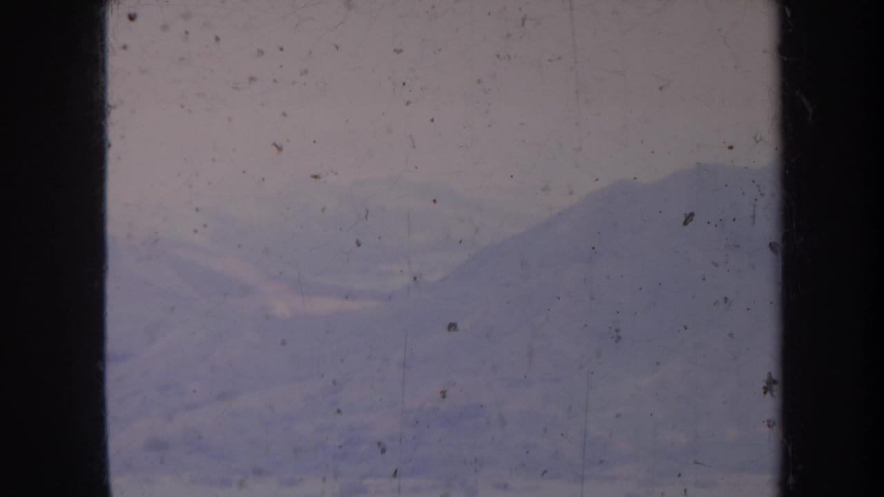 Distant mountain slopes in muted blue tones, framed by dark film edges and surface specks.