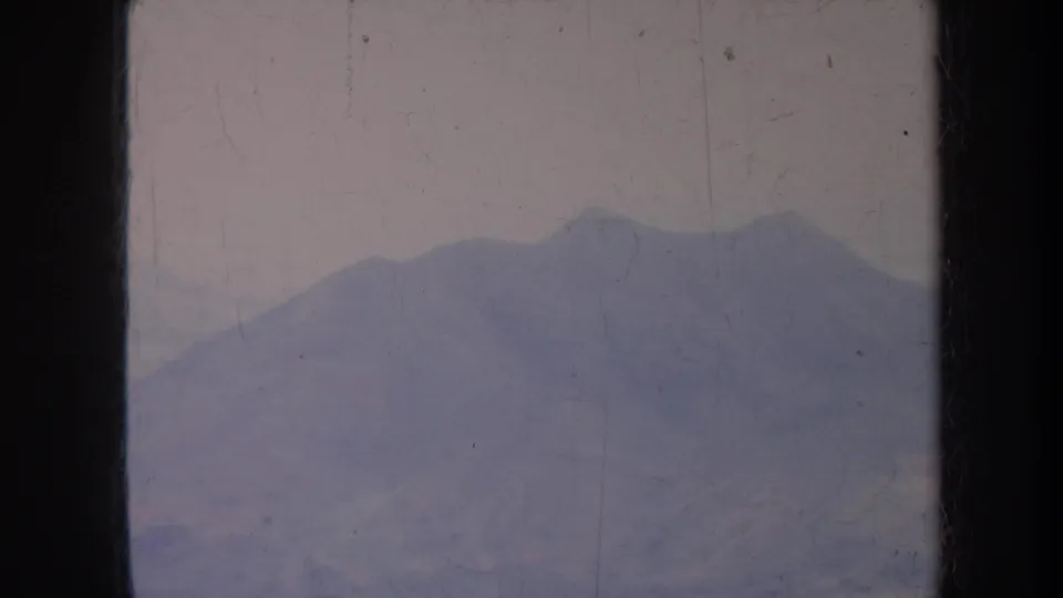 1967 Honolulu 8mm frame showing a hazy mountain silhouette with a faint tree line below, softened by grain, scratches, and uneven exposure.