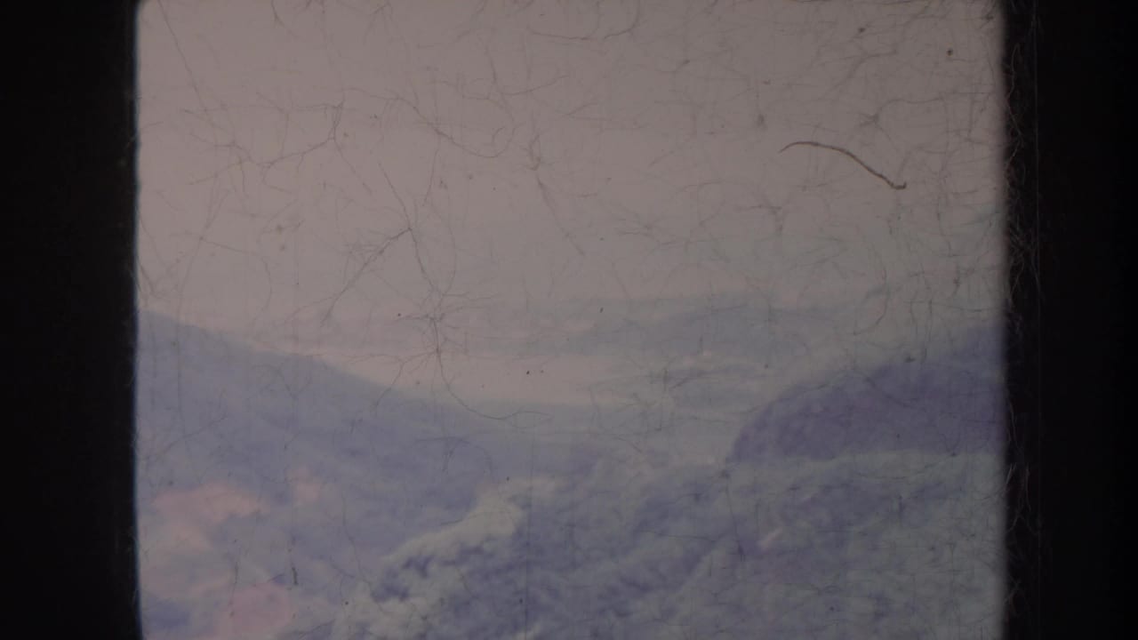 Soft mountain landscape with haze, scratches, dust, and dark film borders.