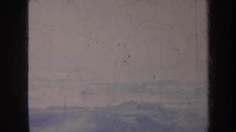 1967 Hawaii home-movie frame showing a pale, hazy mountain view with soft color, dust, scratches, and visible frame edges.