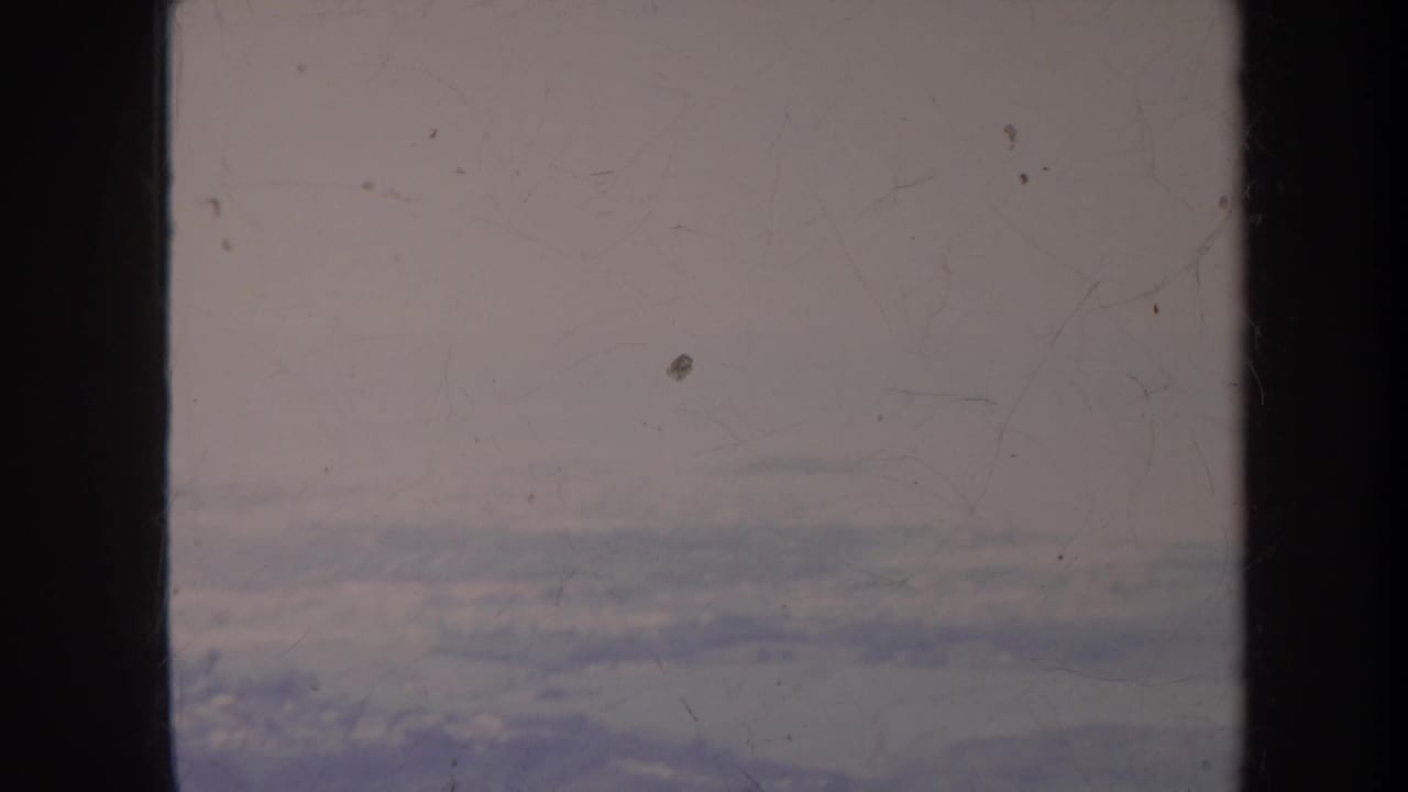 Aircraft-window view over a cloudy horizon with faint landscape visible below.