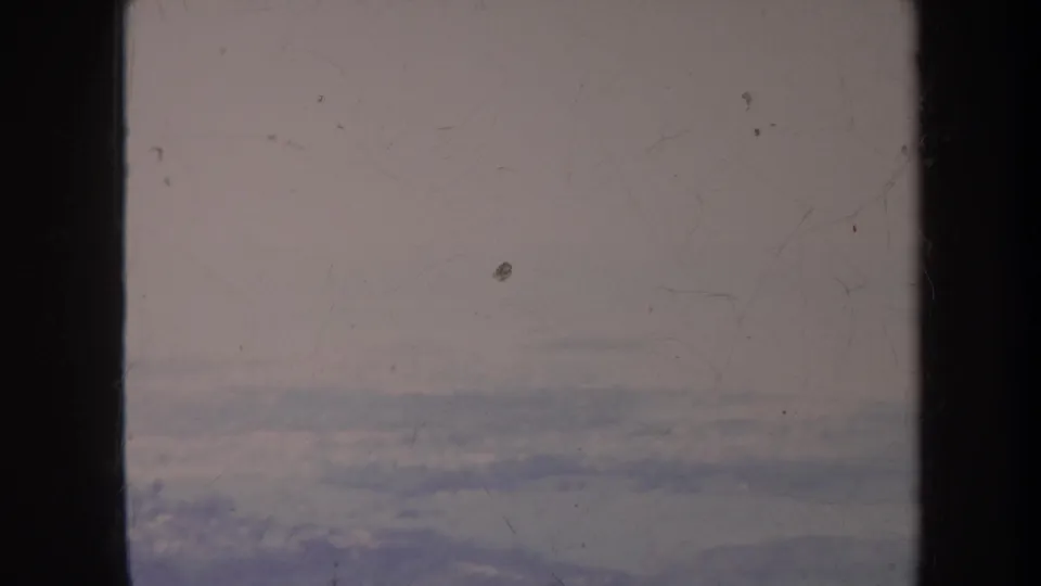 1967 Hawaii aerial frame with dark vertical window dividers, a cloudy horizon, and indistinct terrain beneath the haze.
