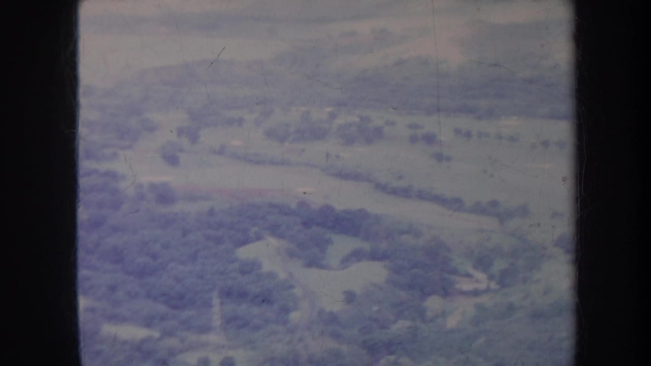 Aerial view of open hills and valleys with scattered trees and dark film borders.