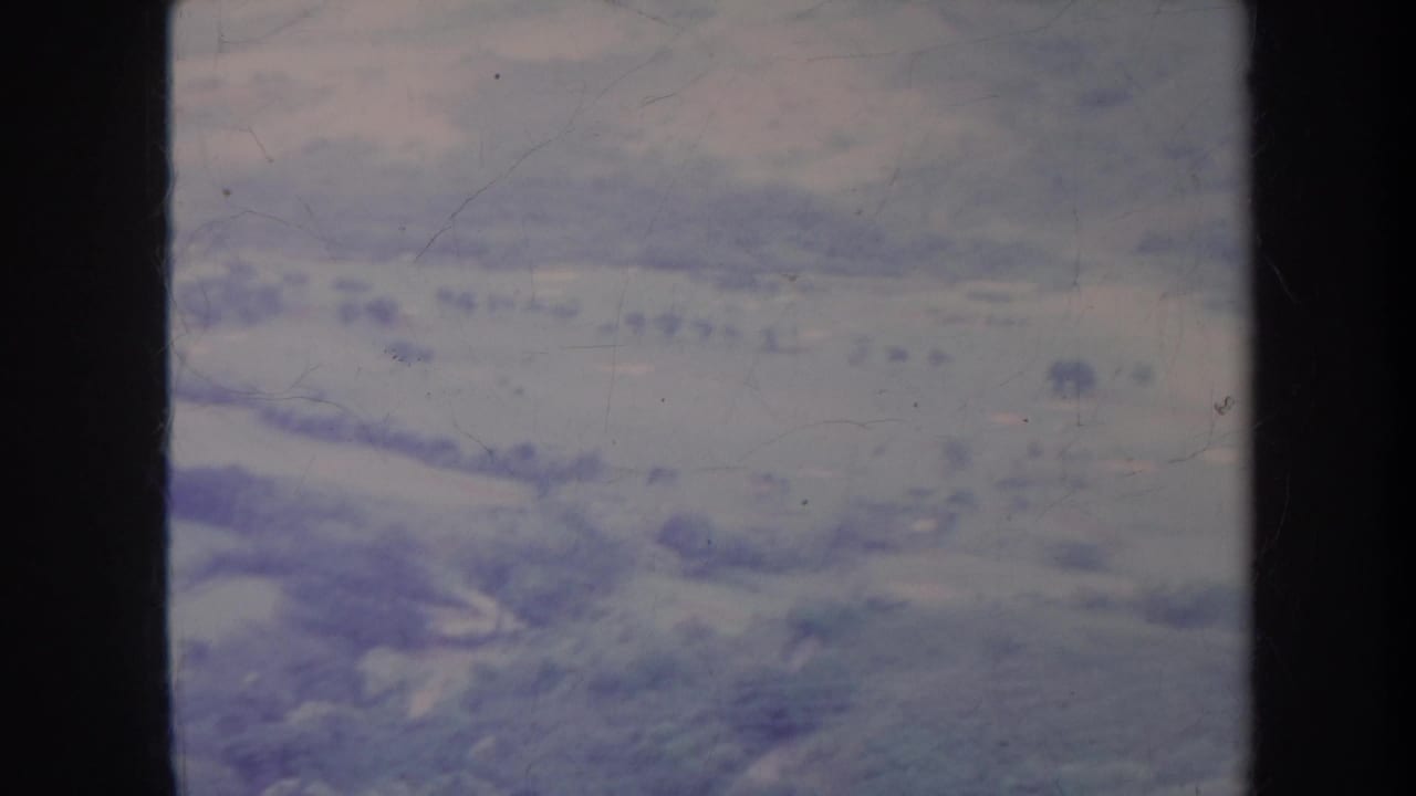 Soft aerial view of pale hillsides, valleys, and scattered foliage under dark film borders.