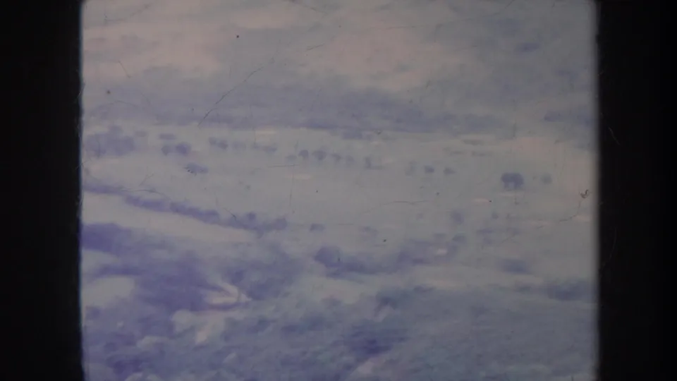 Aerial 8mm view near Honolulu in 1967, with muted hills, scattered vegetation, and visible film wear at the frame edges.