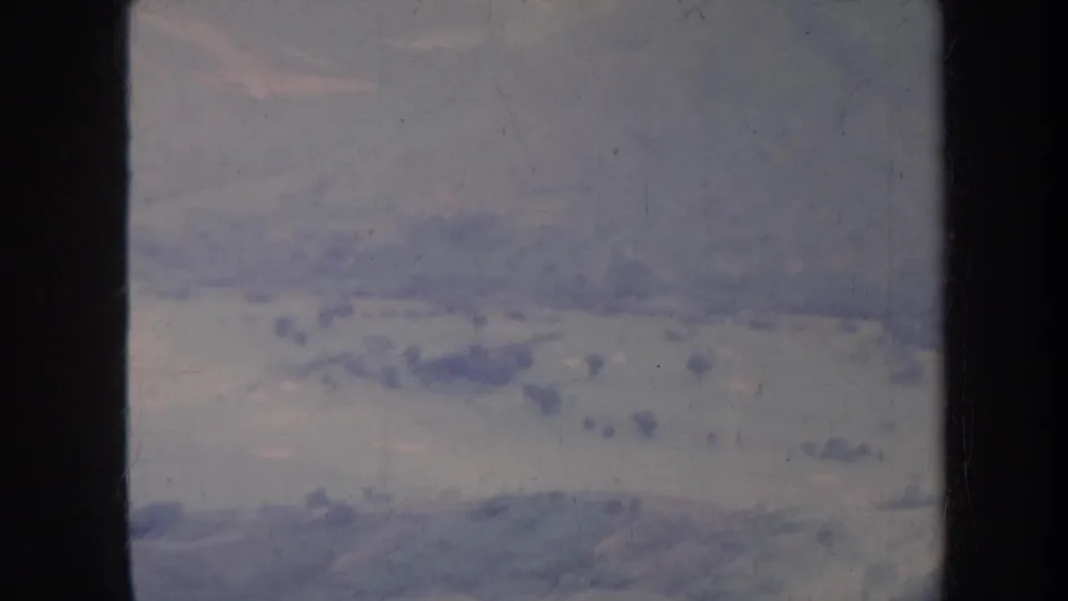 Late-1960s Honolulu-area aerial home-movie frame showing broad open land, low hills, and scattered foliage with aged 8mm texture.