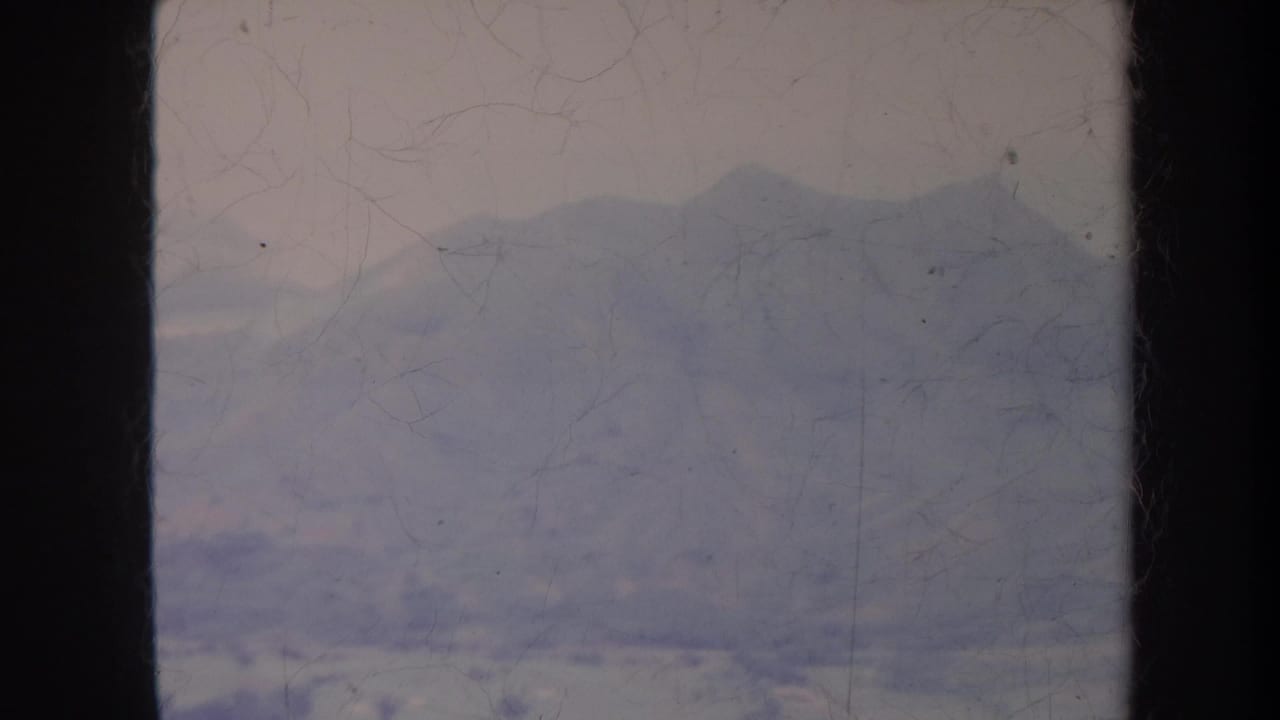 Layered mountain ridges seen through scratched, faded film with dark side borders.