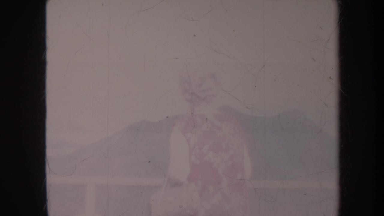 Woman in a floral dress standing near a balcony with hills in the distance.