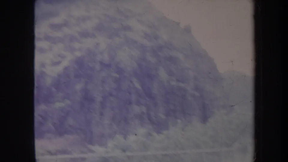 1967 8mm travel footage frame showing a fog-softened mountain slope, dark gate edges, and faded color tones.