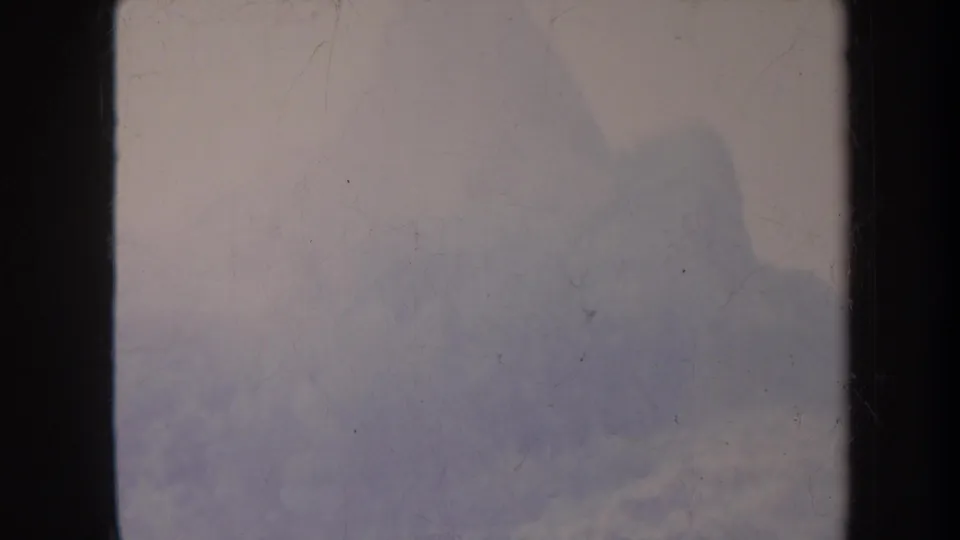 1967 8mm frame with pale fog, faint mountainous shapes, dark vertical gate edges, and visible film wear.