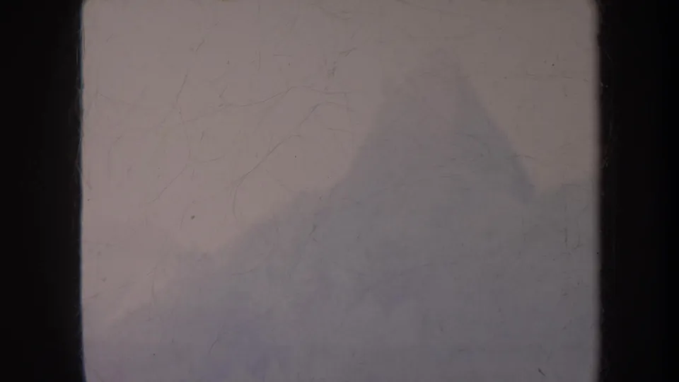 1967 8mm travel frame showing a muted mountain base or slope through fog, with grain and surface scratches visible.