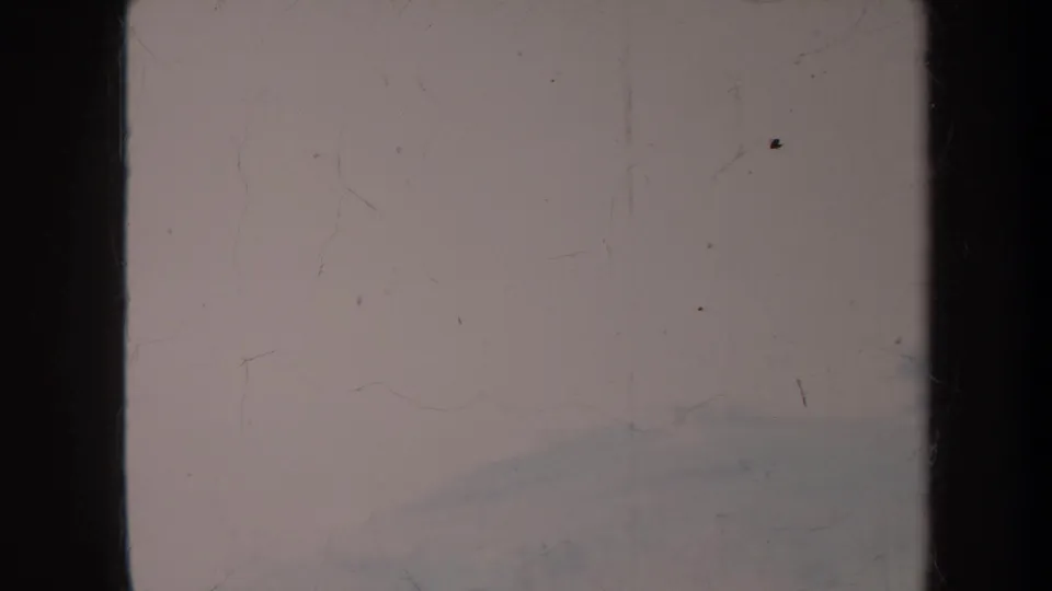 Aged 8mm frame from the 1967 Honolulu clip showing a pale sky, film scratches, dark edges, and a faint distant slope.