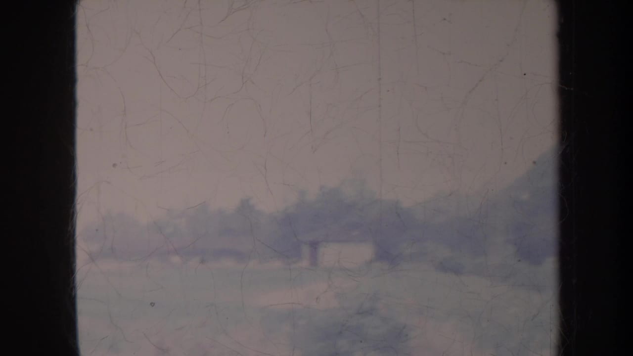 Distant hazy hillside and pale sky seen through scratched film.