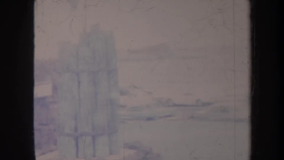 1967 Honolulu home-movie frame showing part of the sign area, a roadside, and distant parked cars through soft faded film.