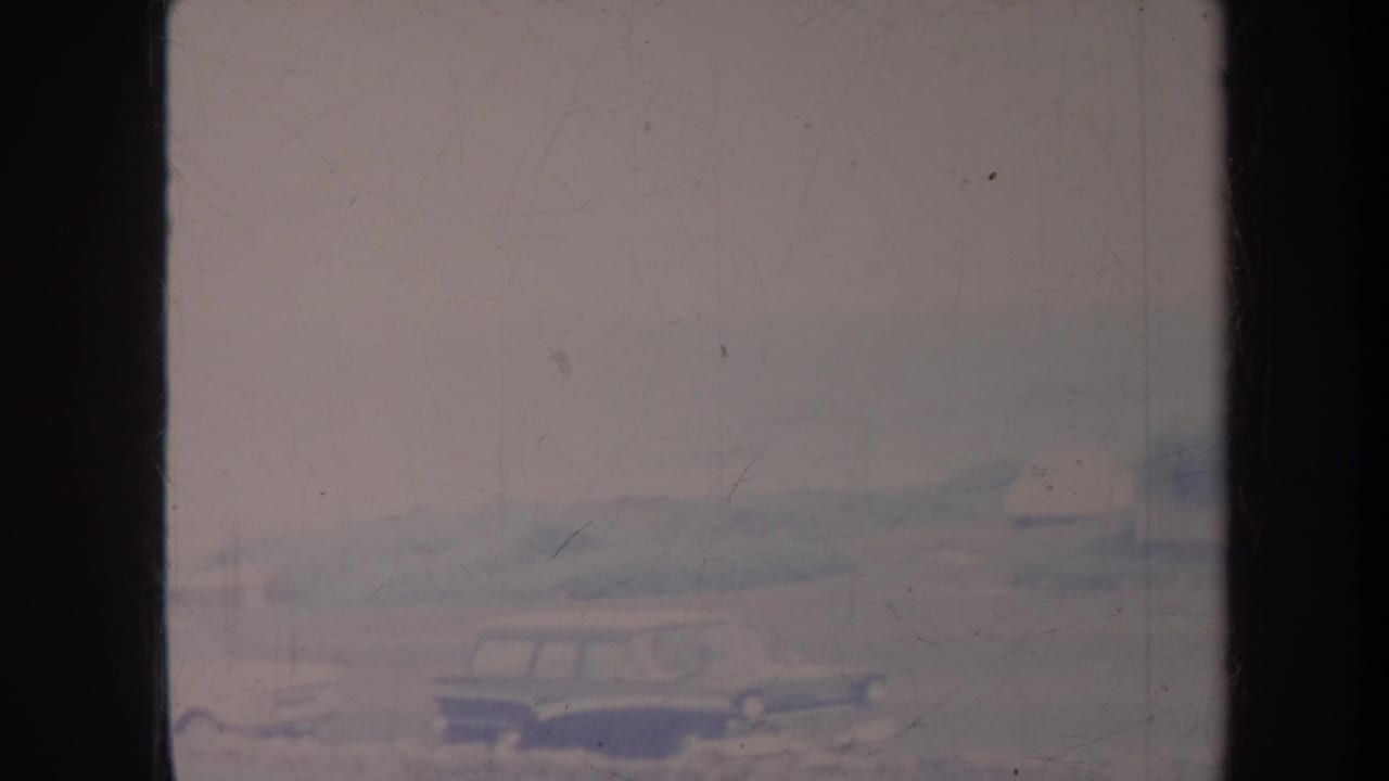 Classic cars on a road seen through a hazy, scratched film frame.