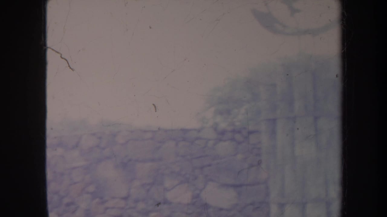 1967 Honolulu frame with rough stone masonry, vertical fence or screen panels, and a soft hillside background in faded 8mm color.