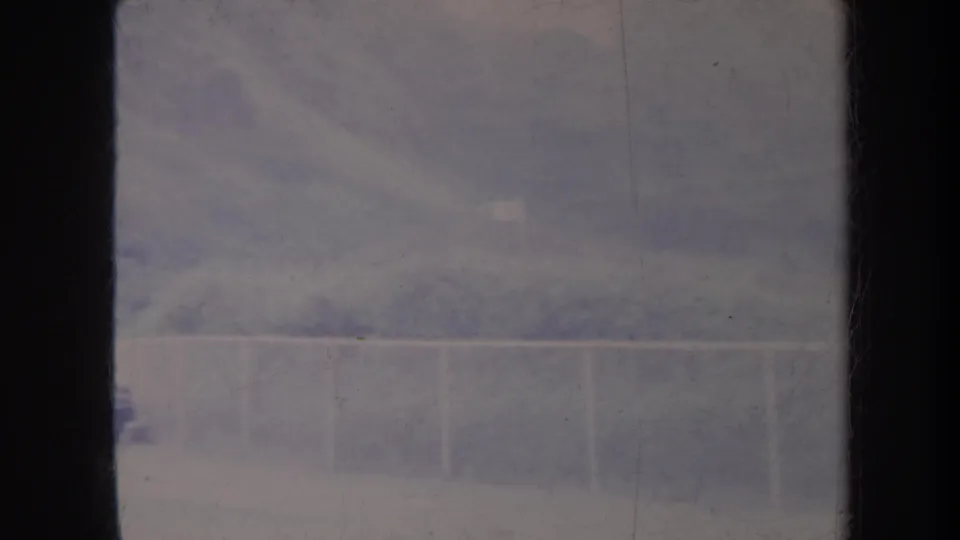 1967 Honolulu 8mm frame with a hazy hillside, pale railing, rough wall texture, and a faint distant vehicle-like shape in soft faded color.