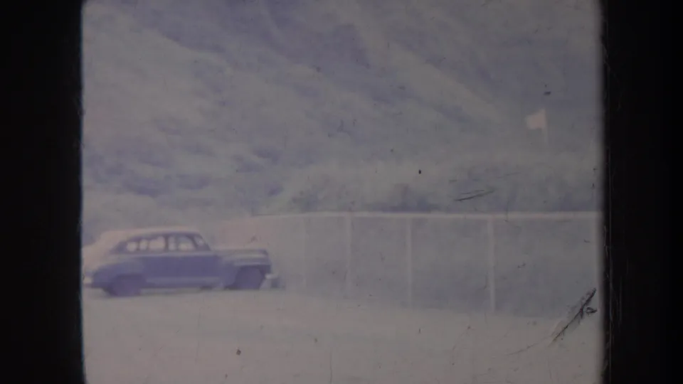 1967 Honolulu 8mm frame showing a blue car near a pale fence below hazy green hills.