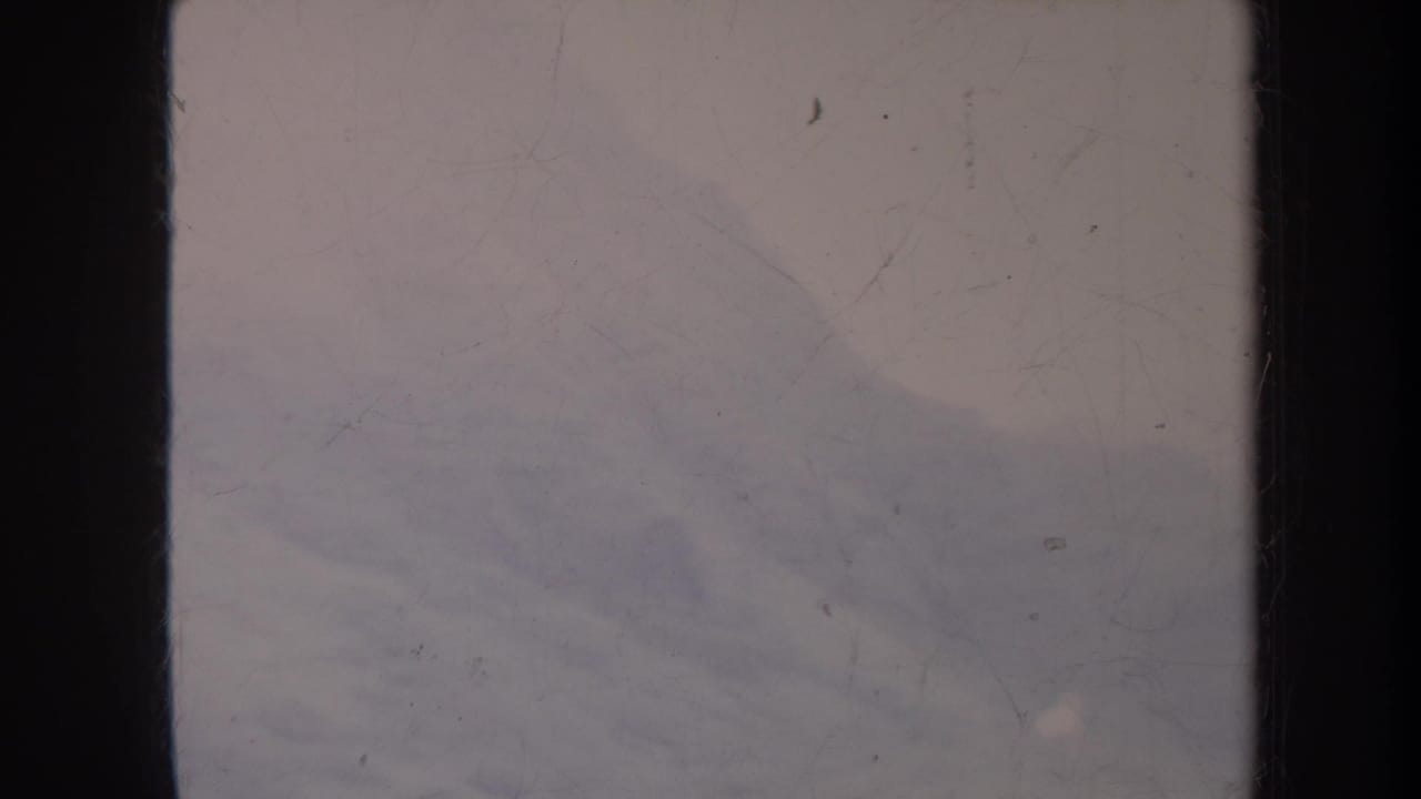 Faded 8mm view of a hazy Honolulu hillside and pale sky, with heavy film wear visible.