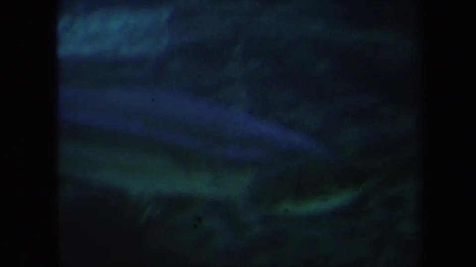 Grainy 8mm footage shows fish forms in a dim Honolulu aquarium tank, with blue-green water and a textured rocky bottom.