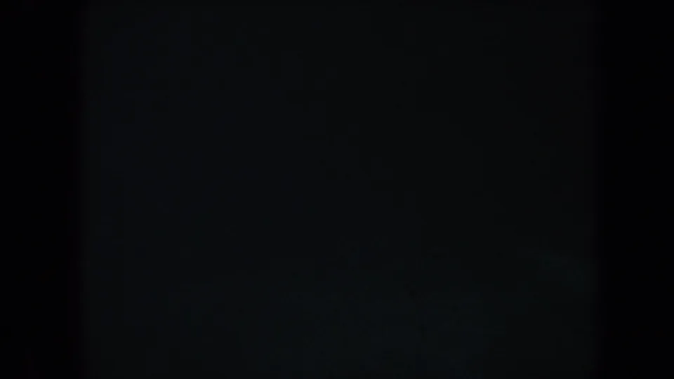 Dark opening frame from 1967 Honolulu underwater 8mm footage, with blue-green water, grain, and very limited reef detail visible.