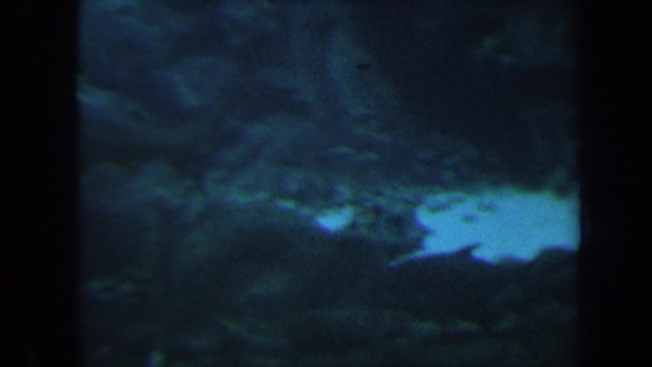 Dim underwater reef area with pale sand patch and dark rock forms.