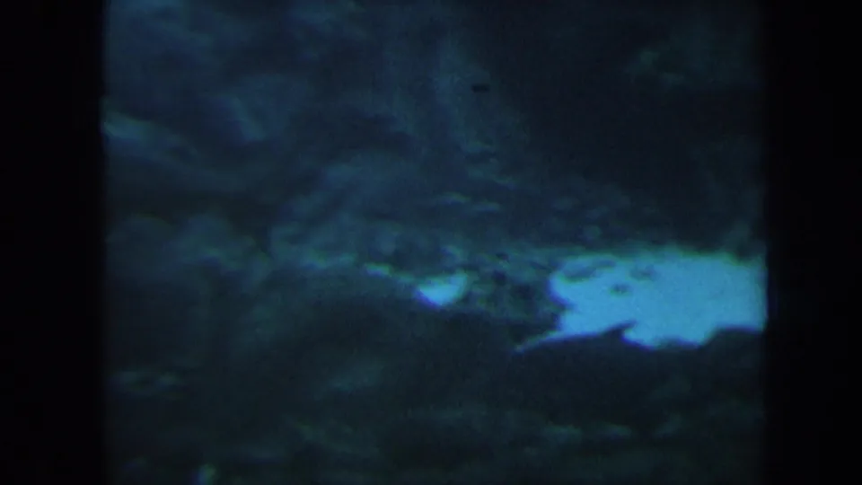 1967 Honolulu underwater frame showing a pale sand patch beside dark reef or lava rock, softened by grain and blue-green water.