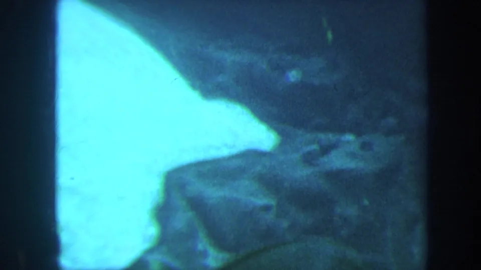 1967 Honolulu underwater 8mm frame with bright sand or light reflecting water at left and darker coral or rock shapes below.