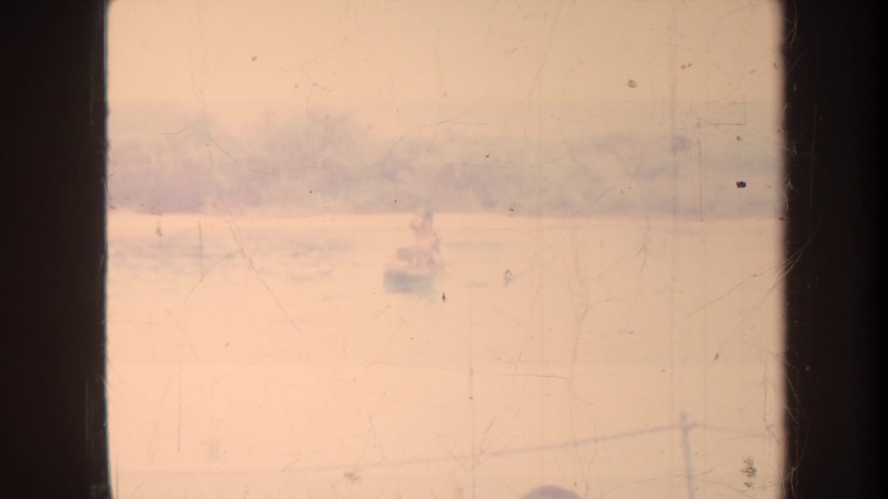 Faded harbor view with small distant boats seen through dark film frame edges.
