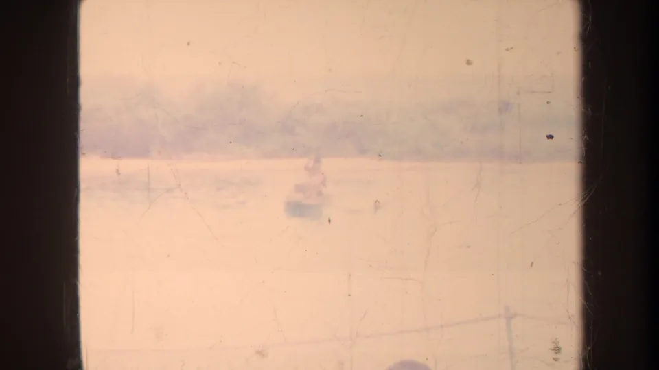 1967 Honolulu home-movie frame showing hazy water and small distant boats, partly obscured by dark vertical frame edges.