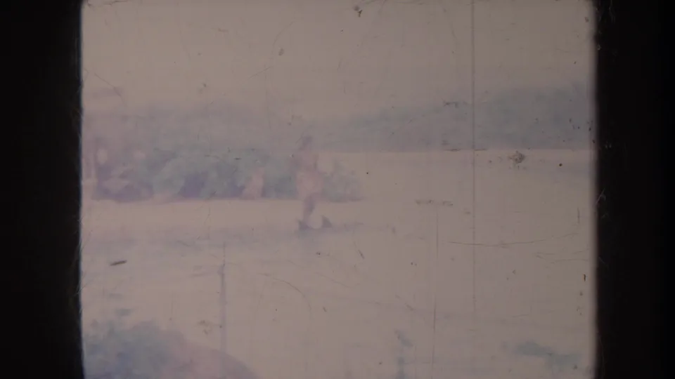 Faded 1967 Honolulu home-movie frame showing calm water and a distant shoreline through heavy 8mm film borders and scratches.