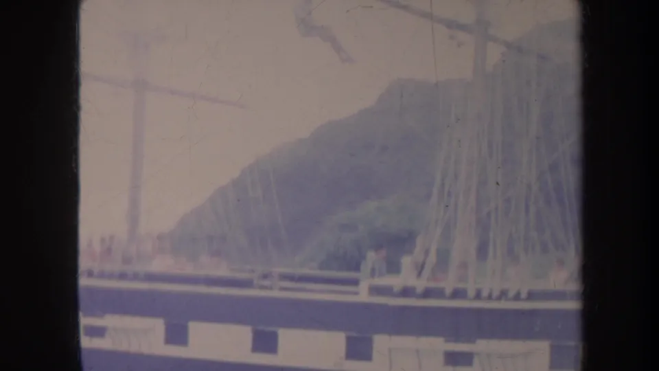 1967 Honolulu frame showing the sailboat deck and rigging against a green hillside, with the waterline low in the frame.