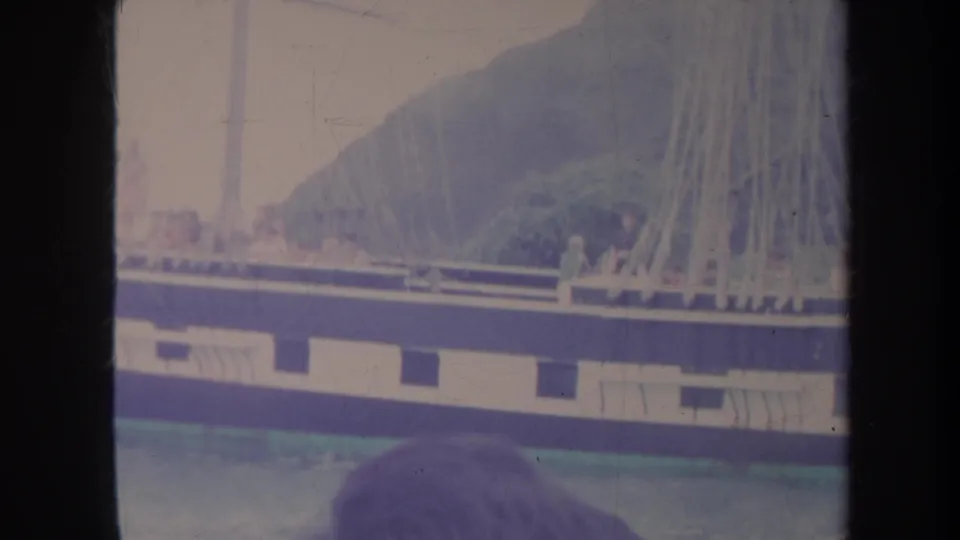 1967 Honolulu home-movie frame with sailboat passengers at the rail, rigging overhead, sea below, and a foreground head at the bottom edge.