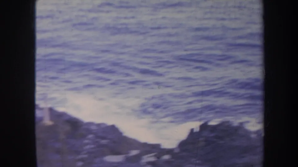 Rough ocean water fills the frame as waves churn near dark shoreline rocks in Honolulu archival 8mm footage.