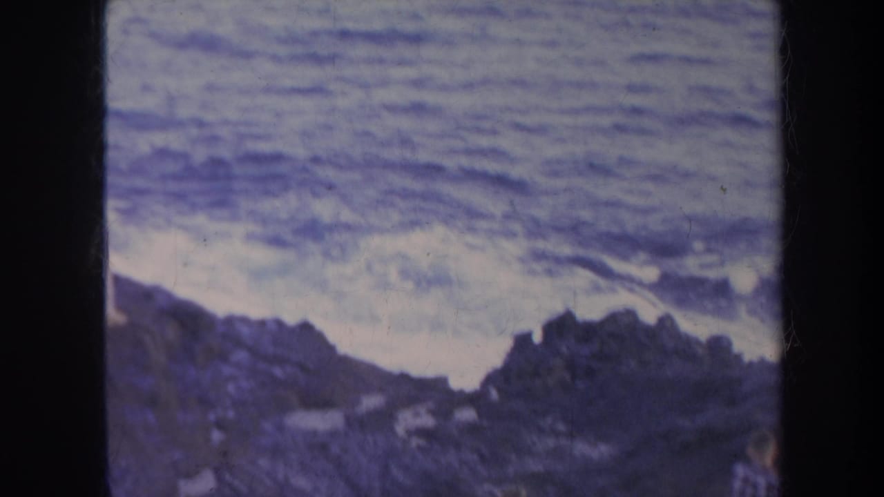 Rocky coastline and ocean seen through a dark 8mm film frame edge.