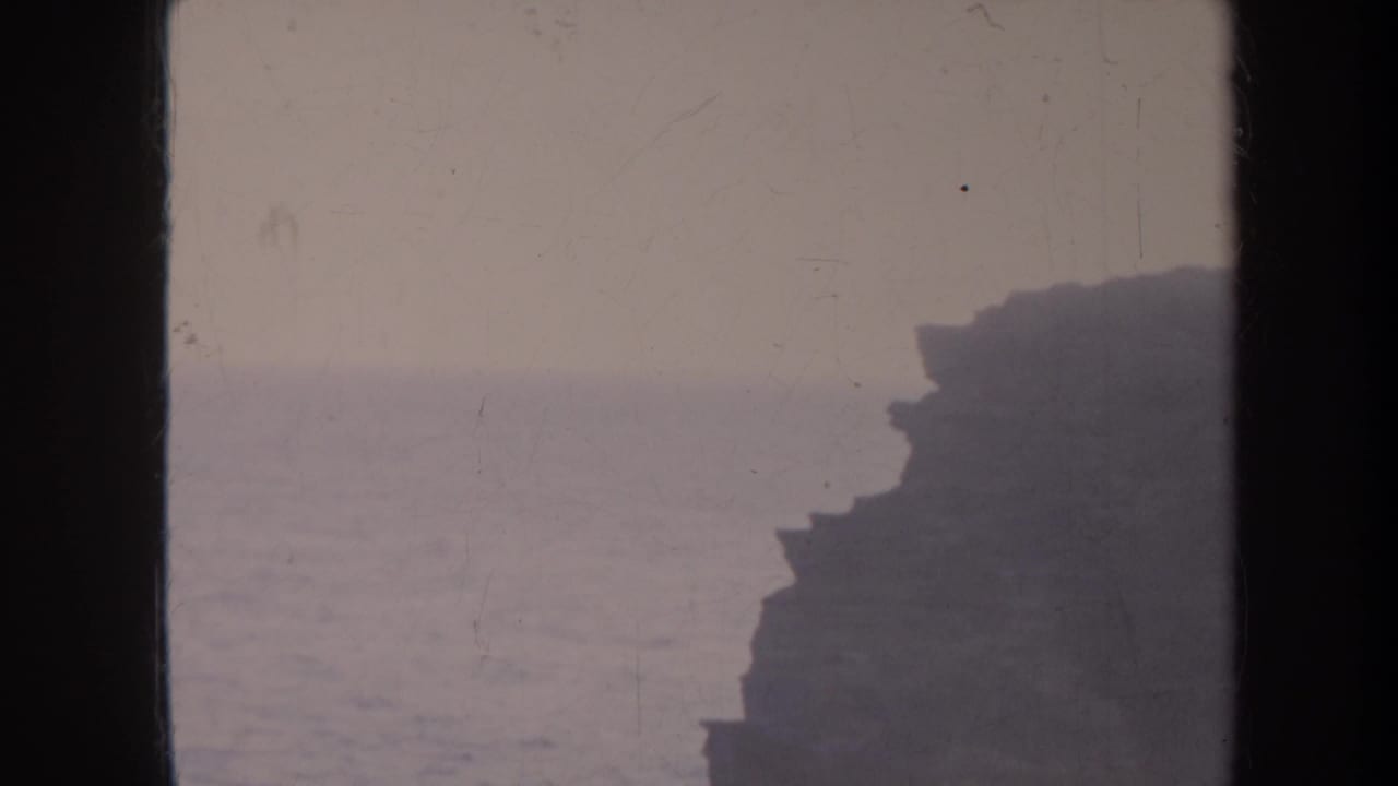 Dark cliff profile beside a hazy ocean horizon.