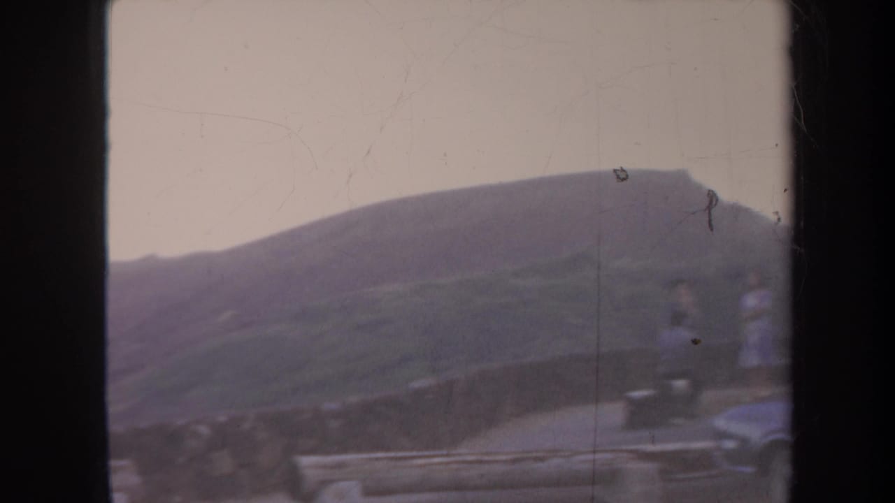 Misty mountain slope and roadside area with small distant people near the right edge.