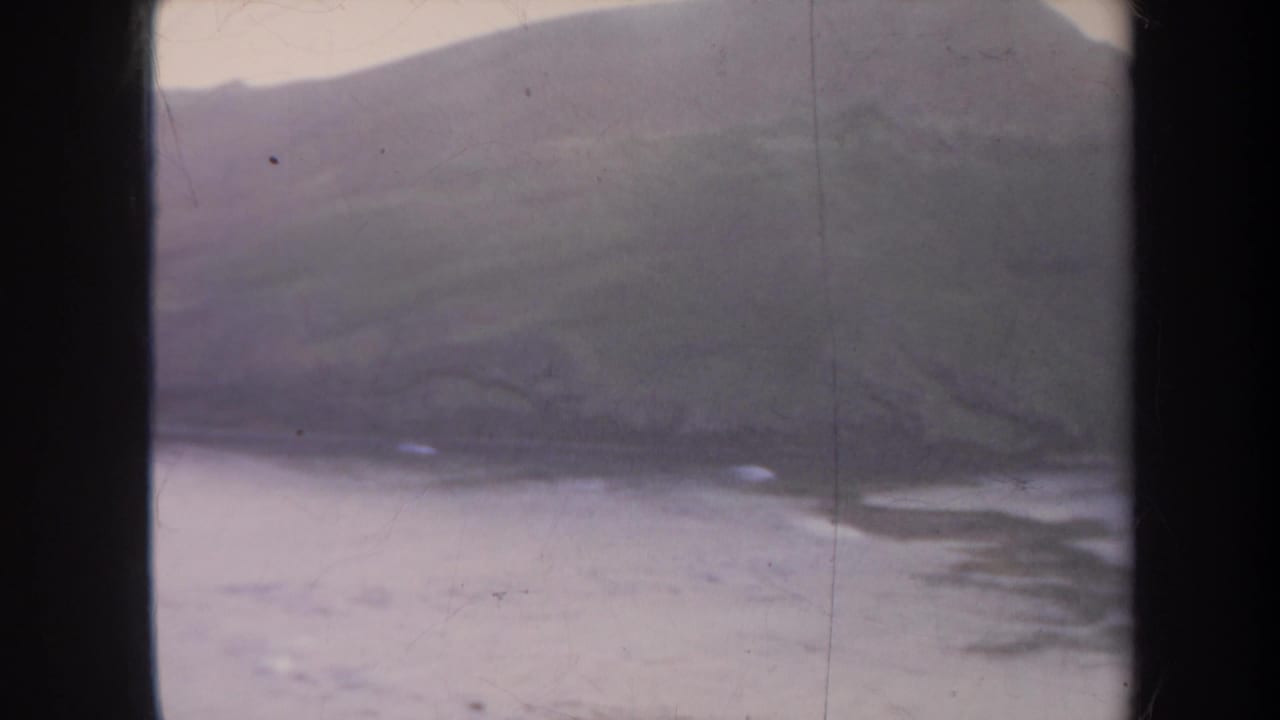 Hillside coastline and calm water with small pale surf patches.