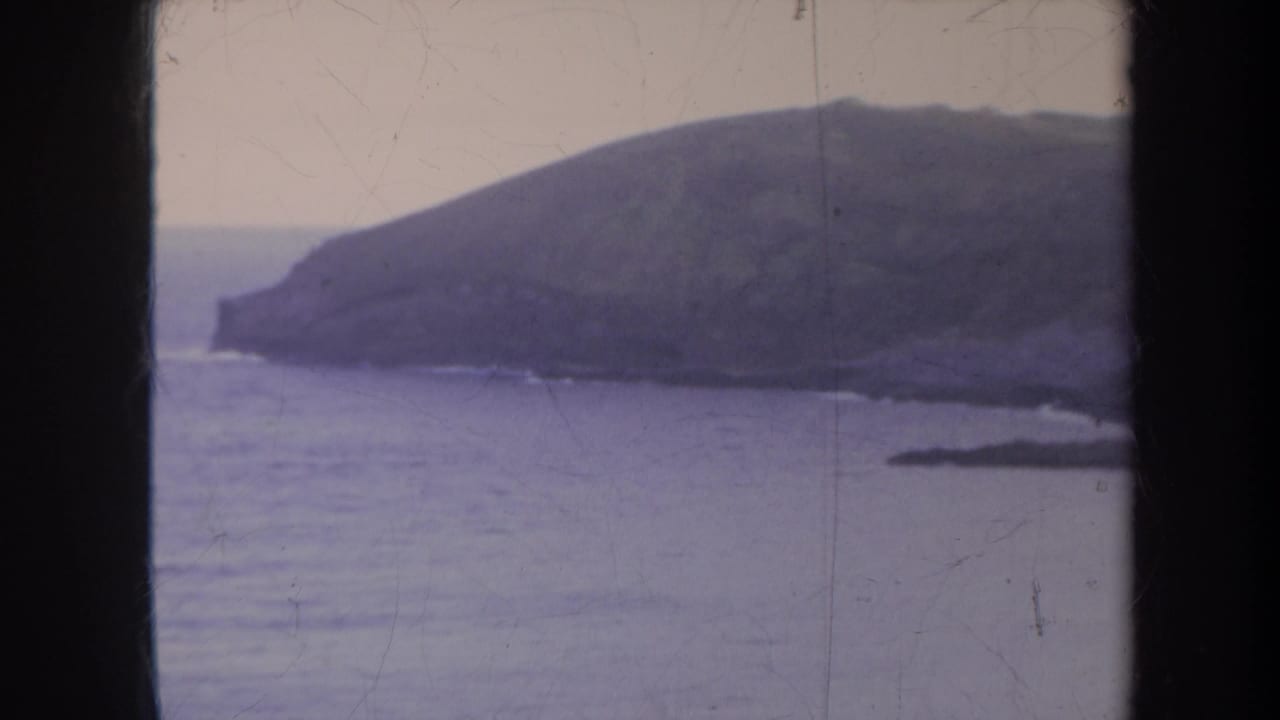 1967 Honolulu-area 8mm frame showing a headland across muted purple water under an overcast sky.