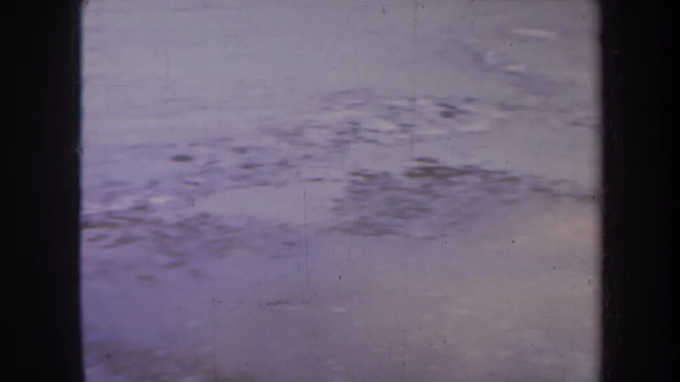 1967 Honolulu-area 8mm frame with soft-focus surf patterns and muted shoreline water.
