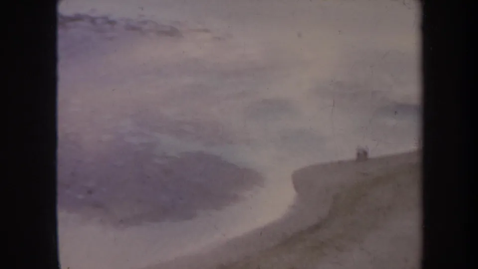 1967 Honolulu-area shoreline with a curving sandy beach, shallow incoming water, and small distant figures.