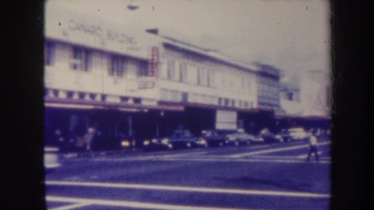 Commercial street corner with parked cars and a pedestrian near the road.