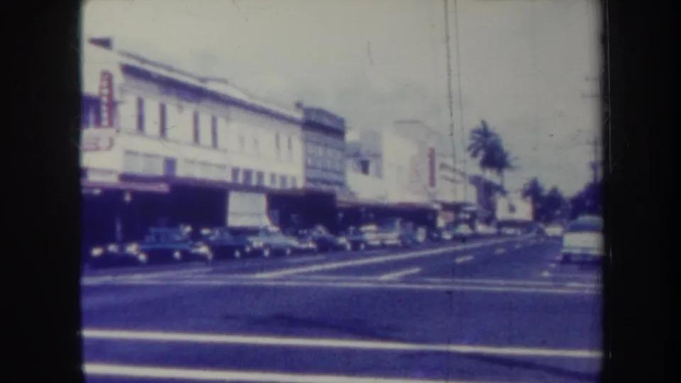 Honolulu commercial street in 1967, showing low-rise buildings, classic cars, lane markings, and palm trees.