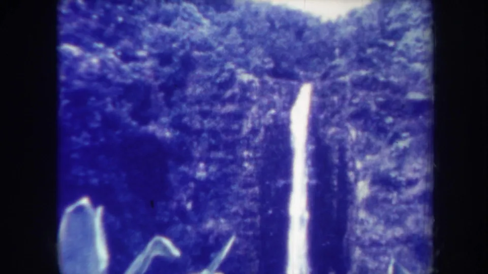 1967 Honolulu 8mm frame showing a tall, narrow waterfall running down a forested rock face, with soft focus, grain, and rounded frame edges.