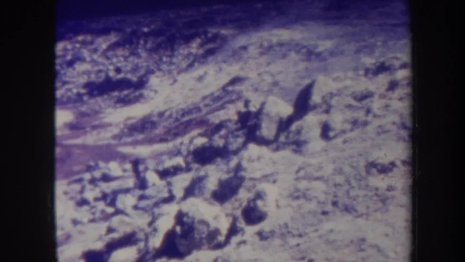 Final 1967 Hawaii frame shifts from the road to rocky ground, showing uneven stones, exposed earth, and strong grain with a blue-purple color cast.